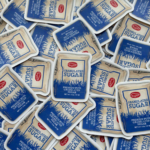 A pile of Bogopa Granulated Sugar bag stickers spread across the frame, showing the blue and white packaging with the red Bogopa logo.